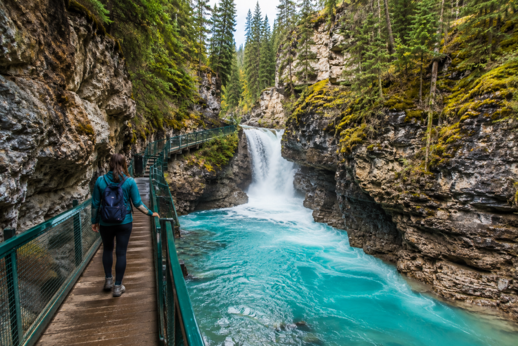 Johnston Canyon waterfall with turquoise river, rocky cliffs, forest, and scenic walking trail in Banff